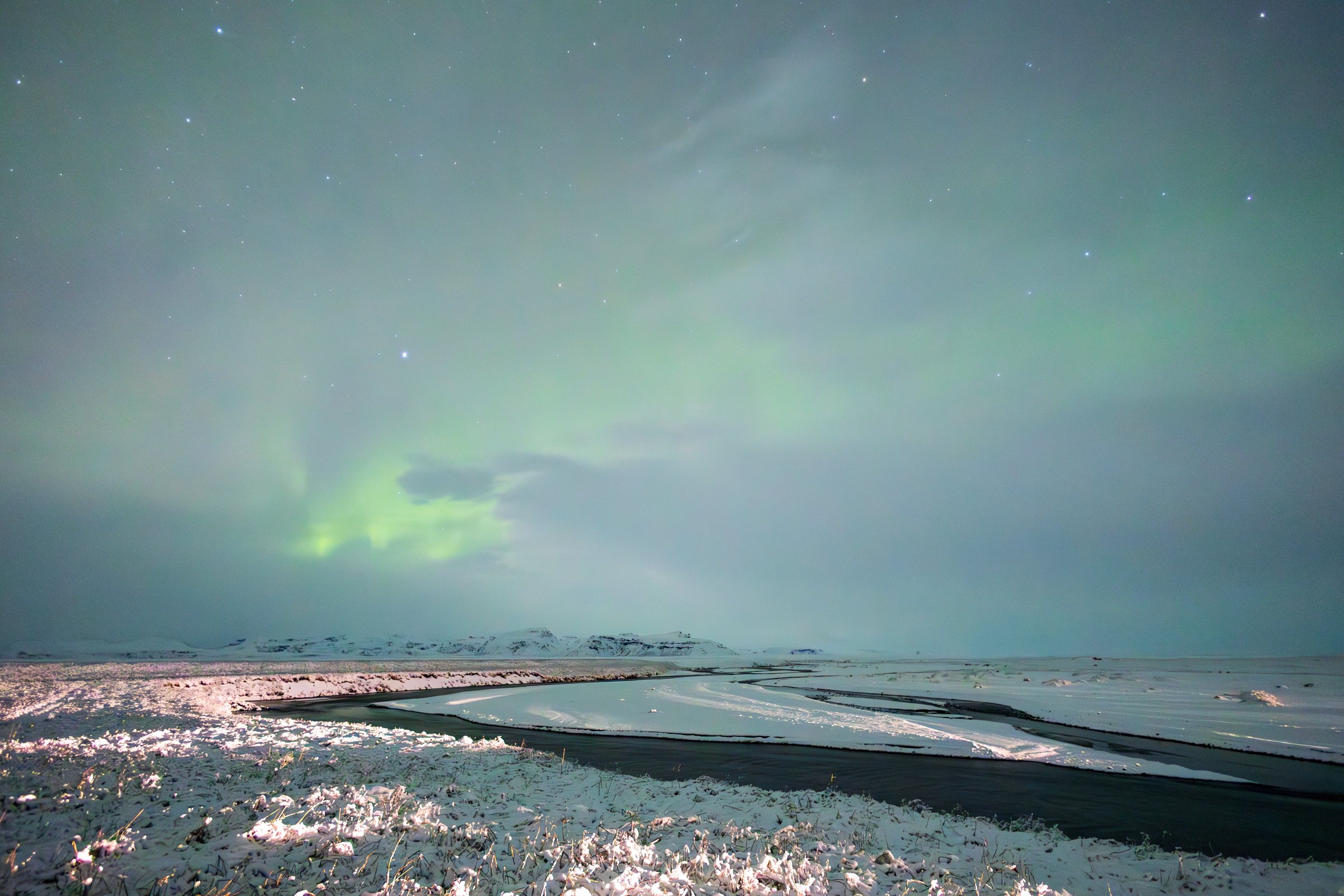 Green aurora hovering above a wintry shoreline